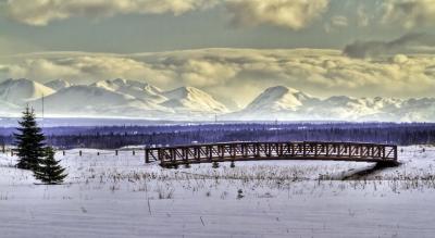 Snowy photo of a bridge in the foreground and mountains in the background.